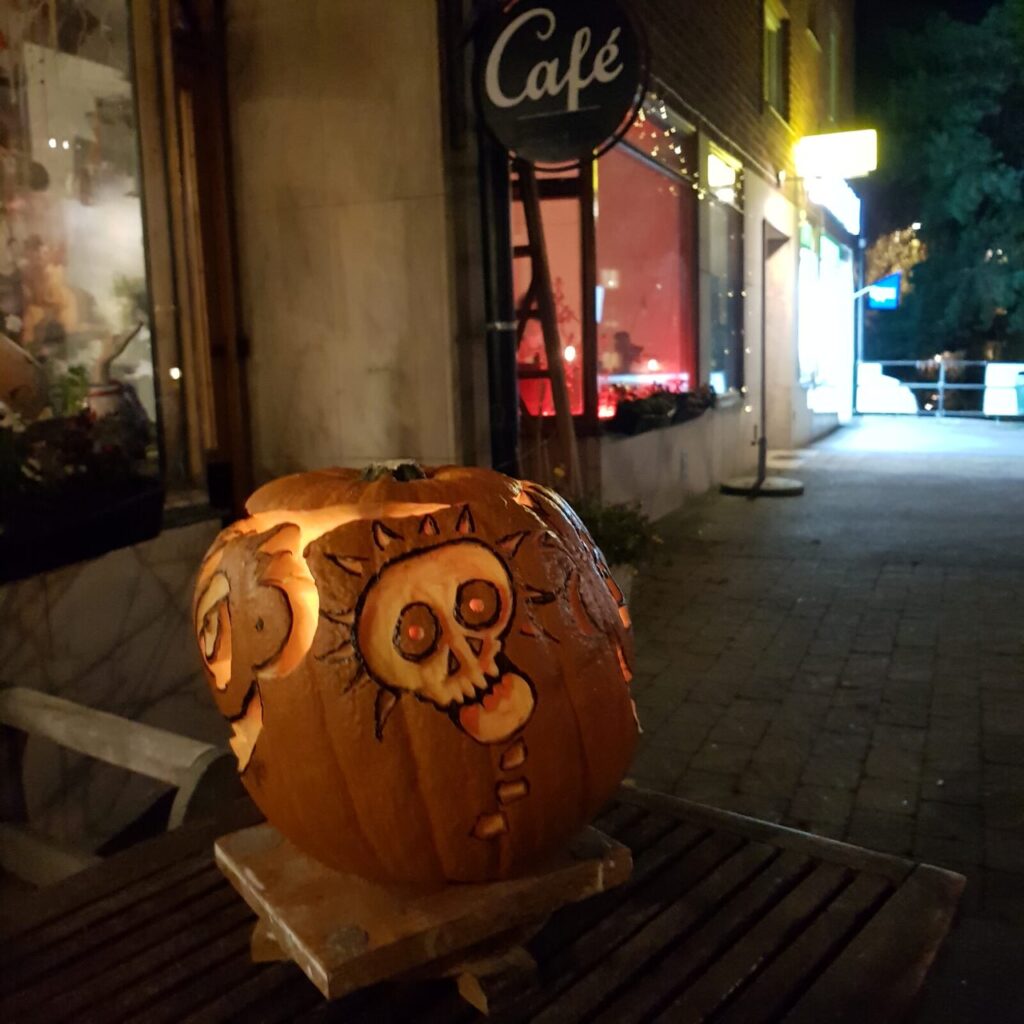 Utskuren pumpa med dödskalle-motiv utanför ett café en höstkväll