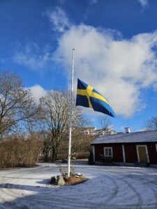 Svensk flagga på halv stång mot blå vinterhimmel
