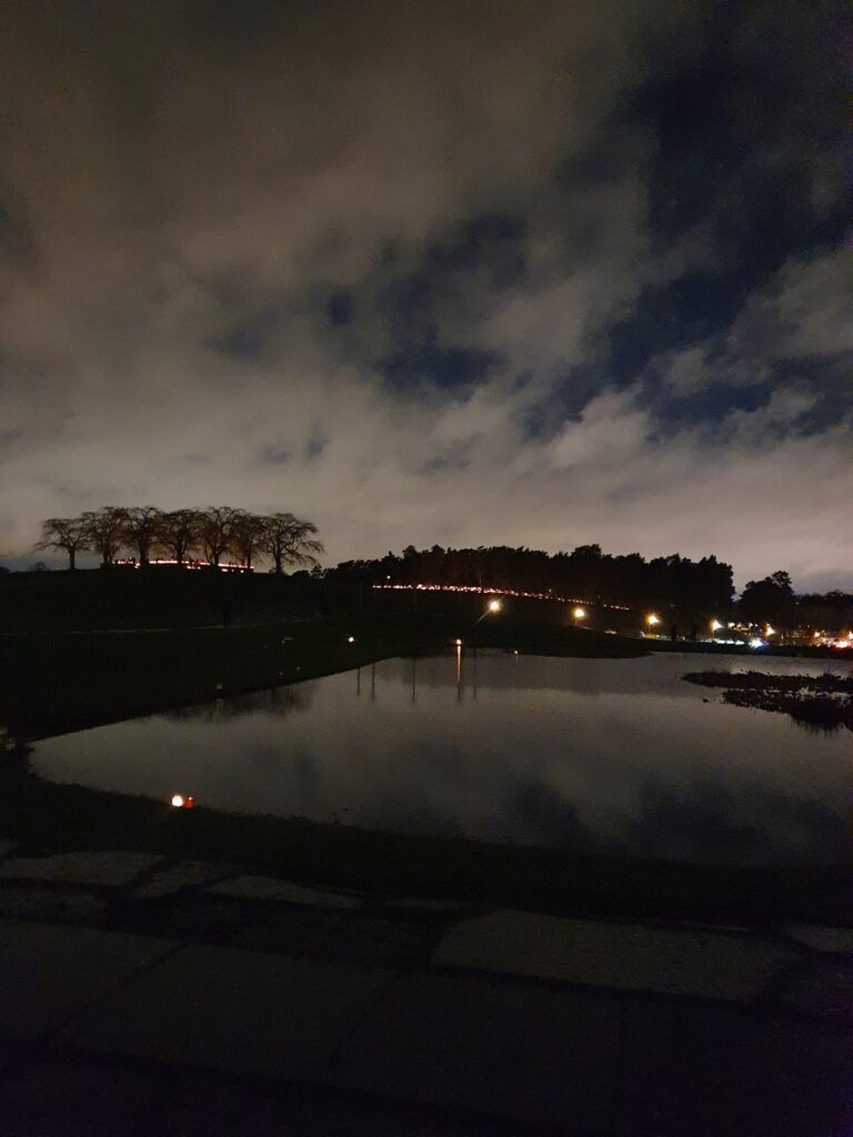 Ljus utplacerade längs en kulle på Skogskyrkogården en kväll, speglade i vatten